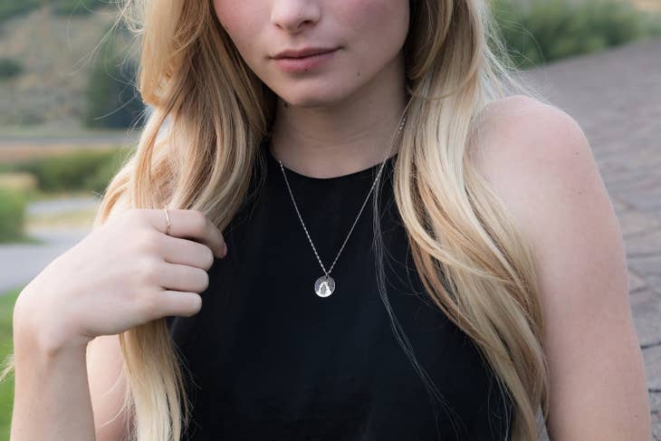 Model wearing the Delicate Arch round pendant necklace on a silver chain over a black top.