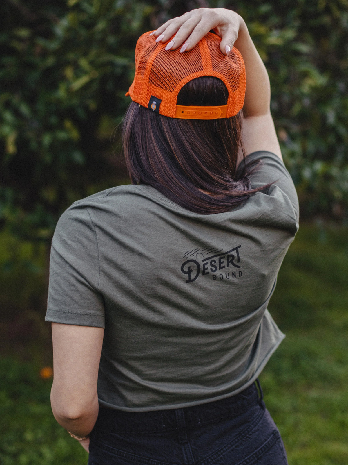 Back view of a person wearing an orange mesh cap with Desert Bound logo on an olive T-shirt.