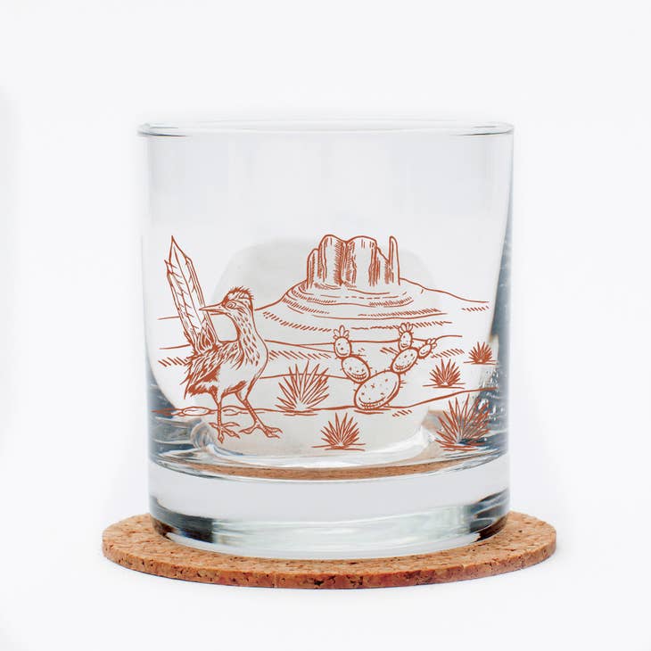 Desert Rocks Glass featuring a red desert illustration with a mesa and cacti on a white background, resting on a cork coaster