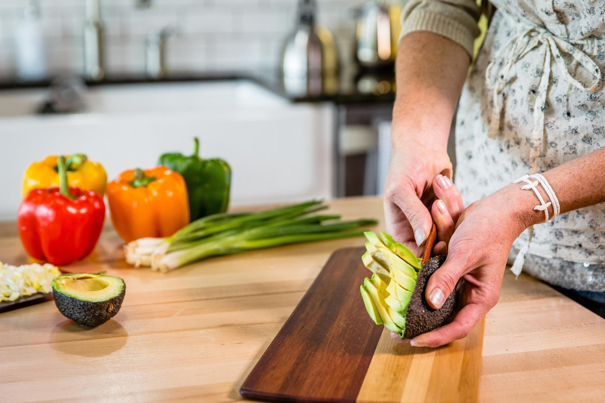 Hands using a dark wooden spreader to spread jam on a cracker with a jam jar and bread on the board