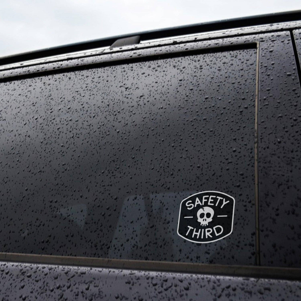 Safety Third sticker on a dark car window with raindrops and partial view of the sticker
