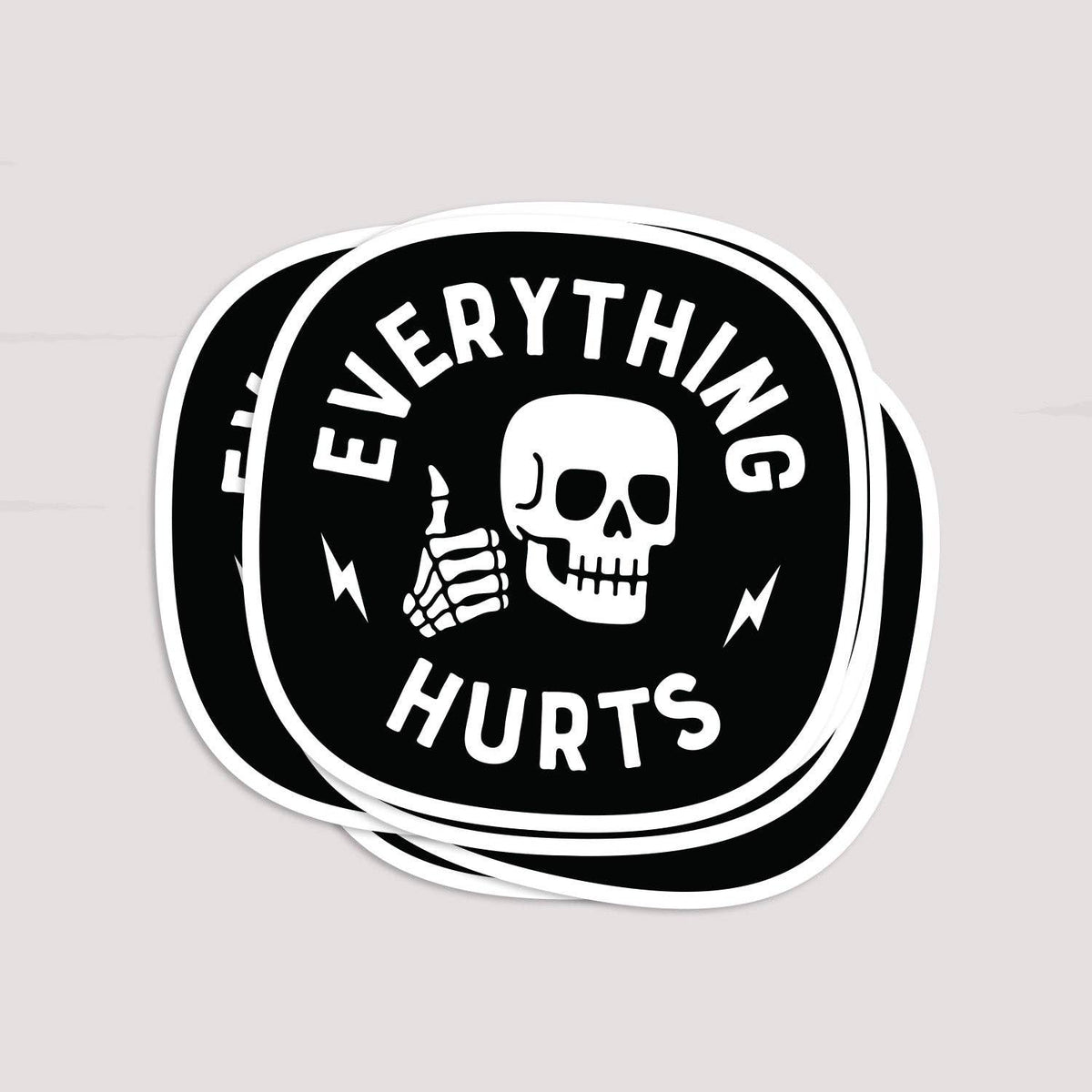 Stack of black circular Everything Hurts stickers with a white skull on a light gray background