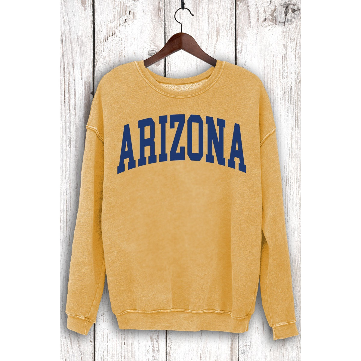 Mustard yellow Arizona mineral wash sweatshirt hanging on a wooden hanger against weathered white wood.