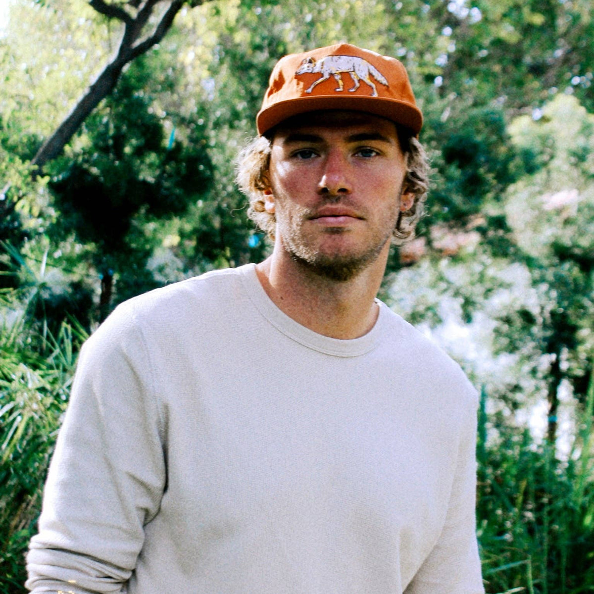 Man wearing The Coyote Hat outdoors with green foliage in the background