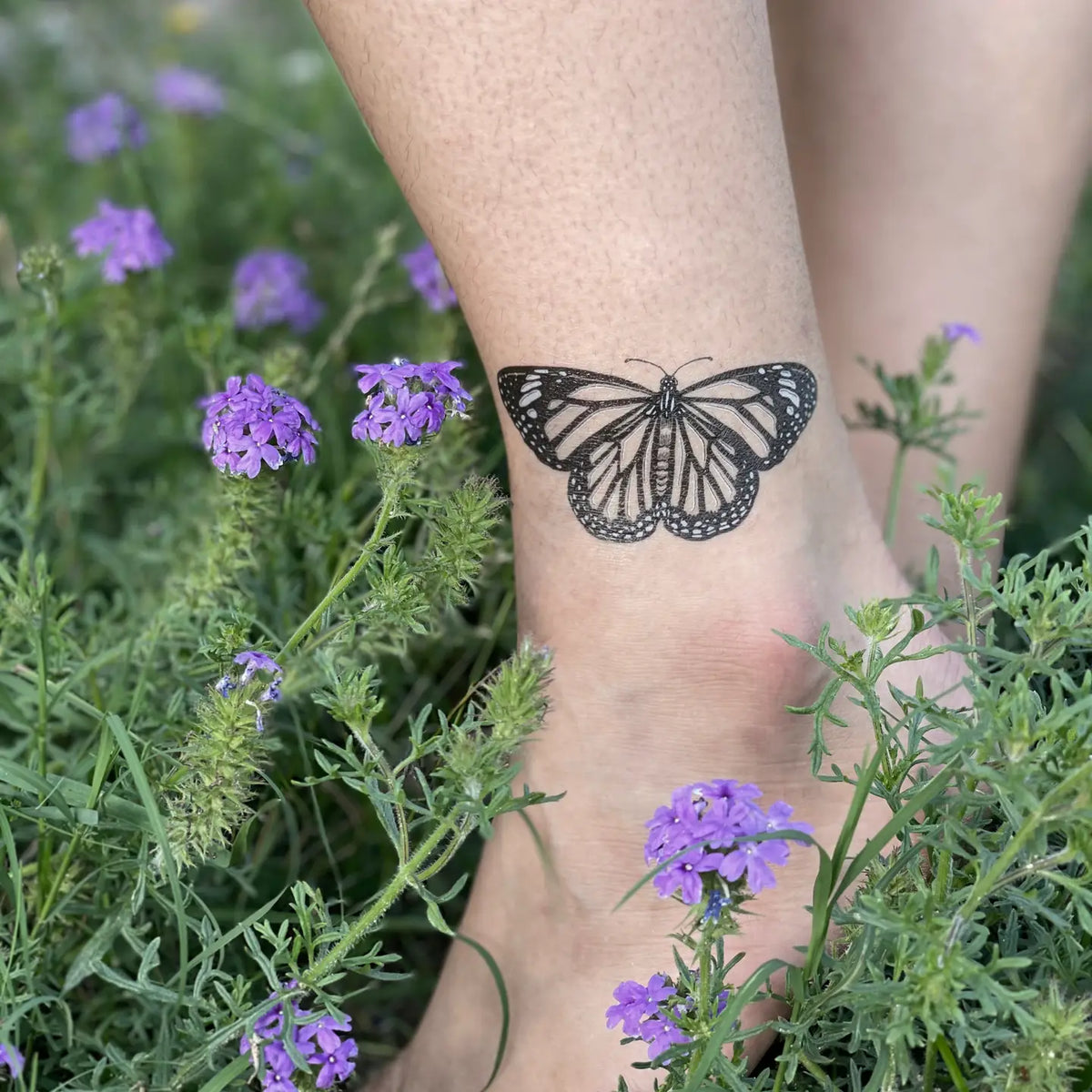 Monarch butterfly temporary tattoo on the ankle surrounded by purple wildflowers.