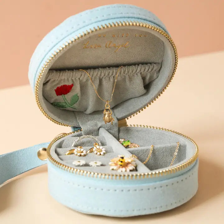 Open light blue velvet round jewelry case with gold zipper displaying flower embroidered lining and jewelry inside