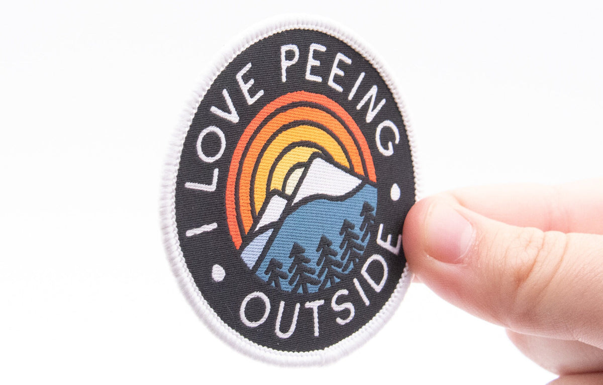 Close up of I Love Peeing Outside patch being held by fingers showing the mountain sunset design