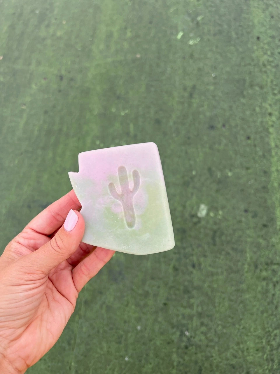 Pastel prickly pear soap with cactus cutout held outdoors over green grass.