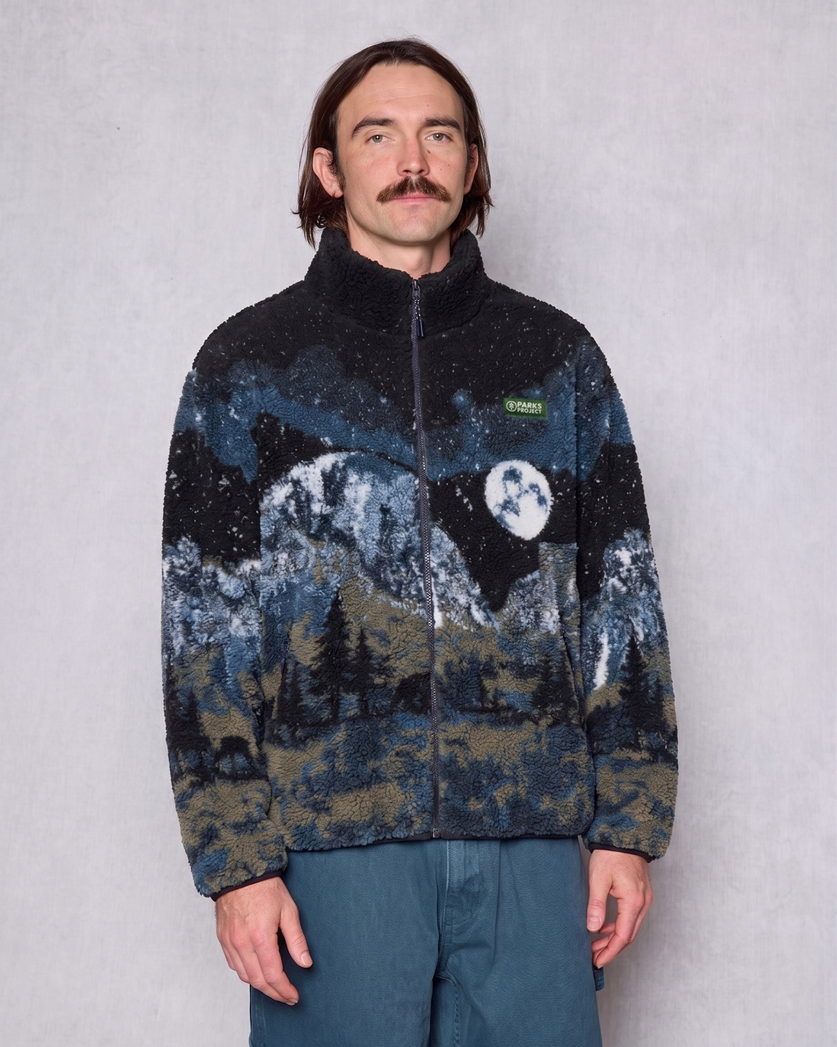 Front view of a man wearing a zipped Yosemite Night Views fleece with mountain print and Parks Project patch
