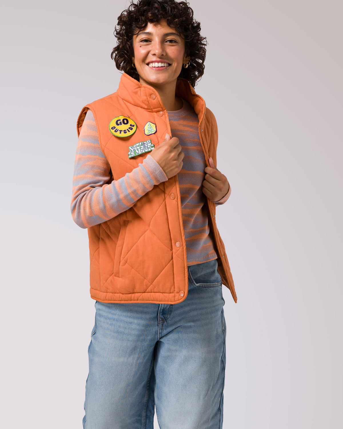 Smiling woman wearing an orange quilted puffer vest with patches on the chest.