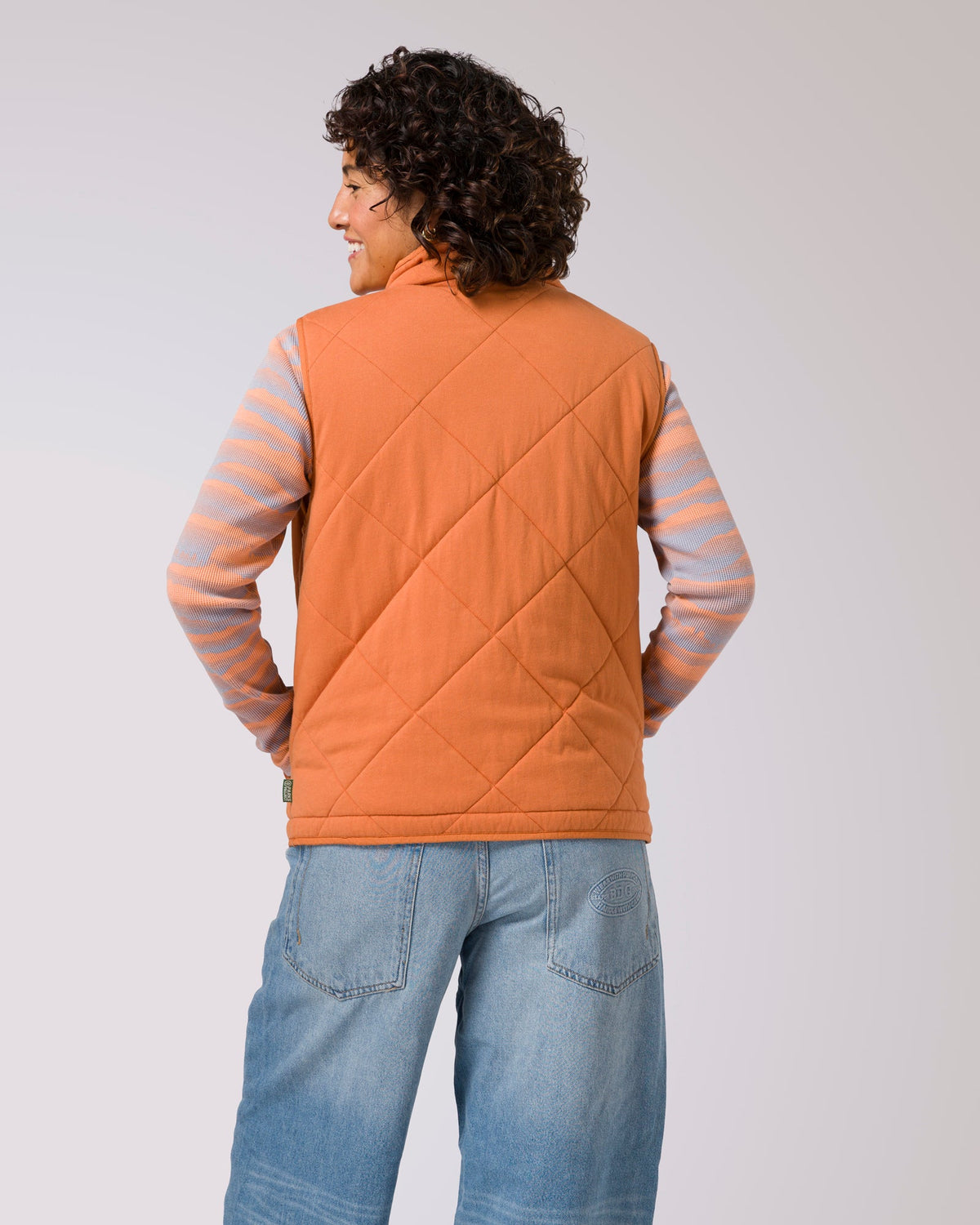 Back view of an orange quilted puffer vest worn by a woman.