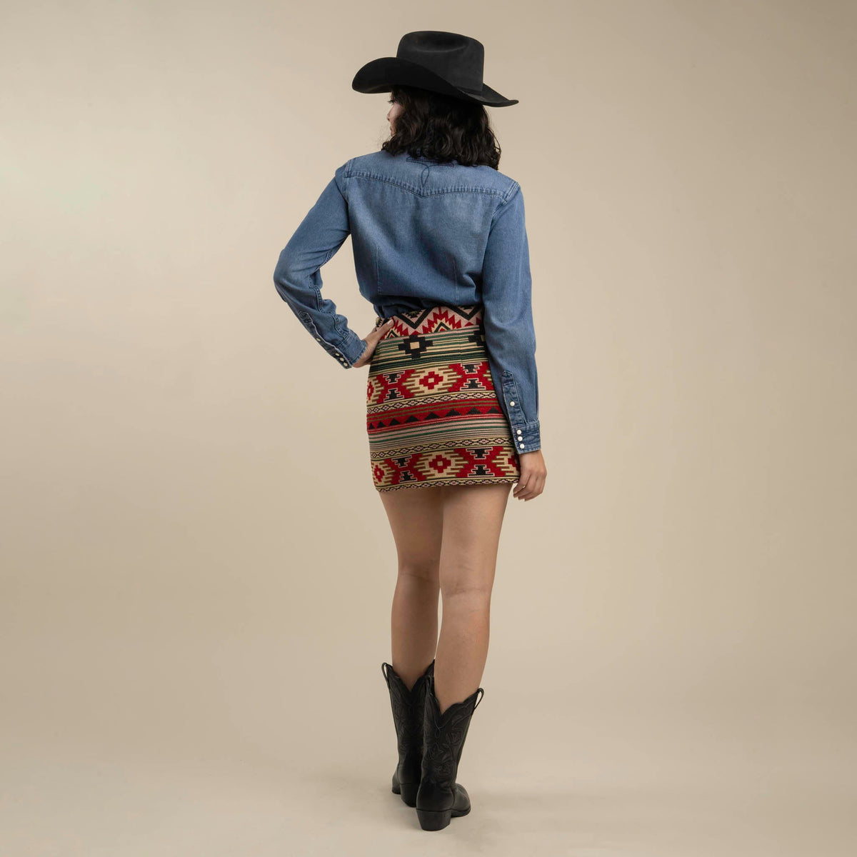 Back view of a model wearing The Raquel Skirt with a blue denim shirt and black boots.