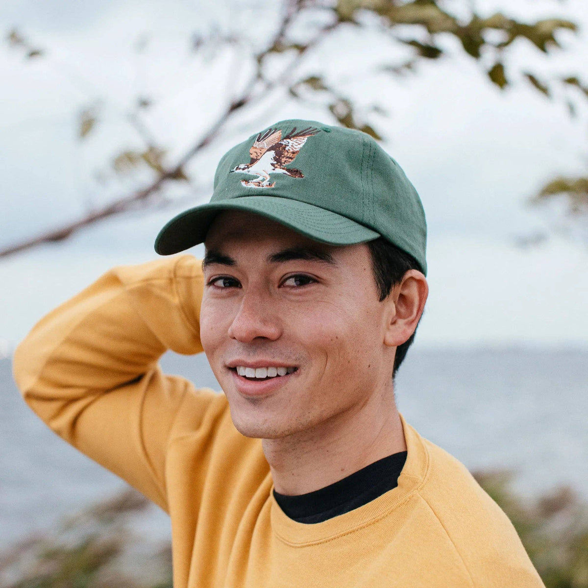 Close-up of a person wearing a green Osprey hat with an embroidered bird emblem