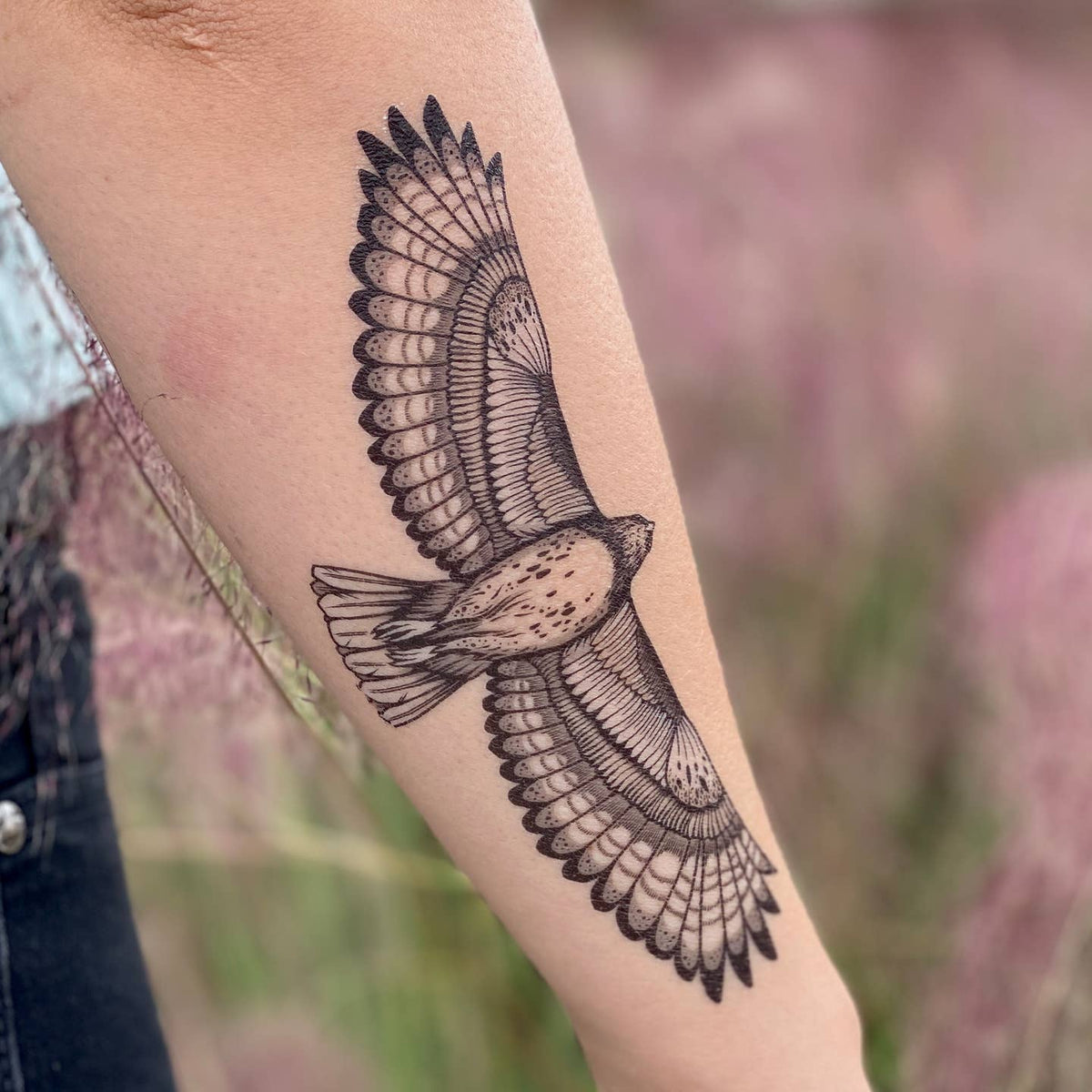 Intricate hawk wings tattoo wrapping around the forearm.