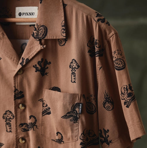Close up of brown desert print casual button up with black icons and chest pocket, Pyknic label visible on hanger