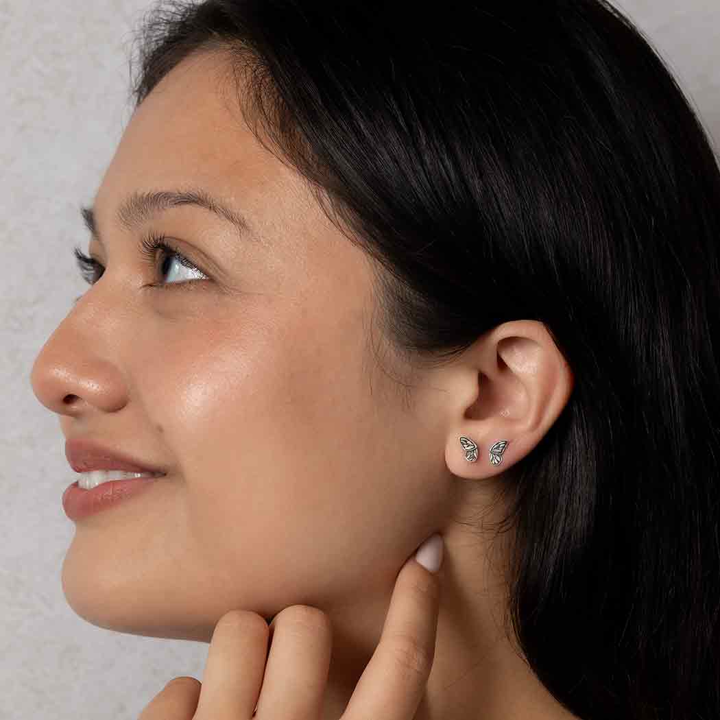 Close up of a woman wearing two tiny butterfly wing stud earrings on the earlobe.