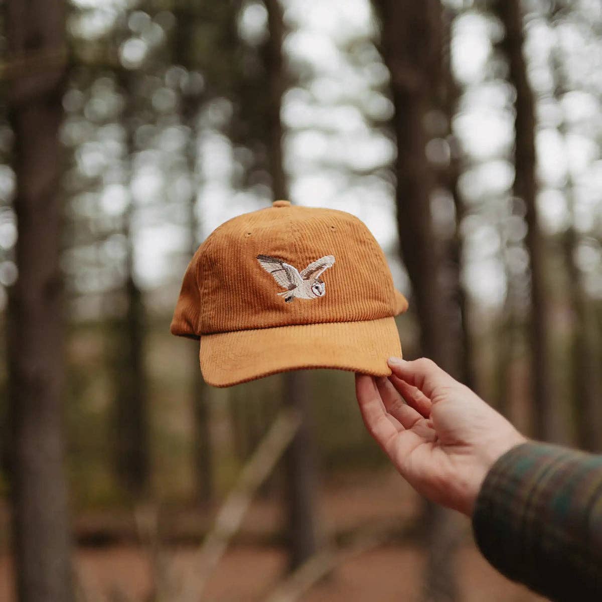 Holding orange corduroy Barn Owl hat with embroidered owl in a forest setting.