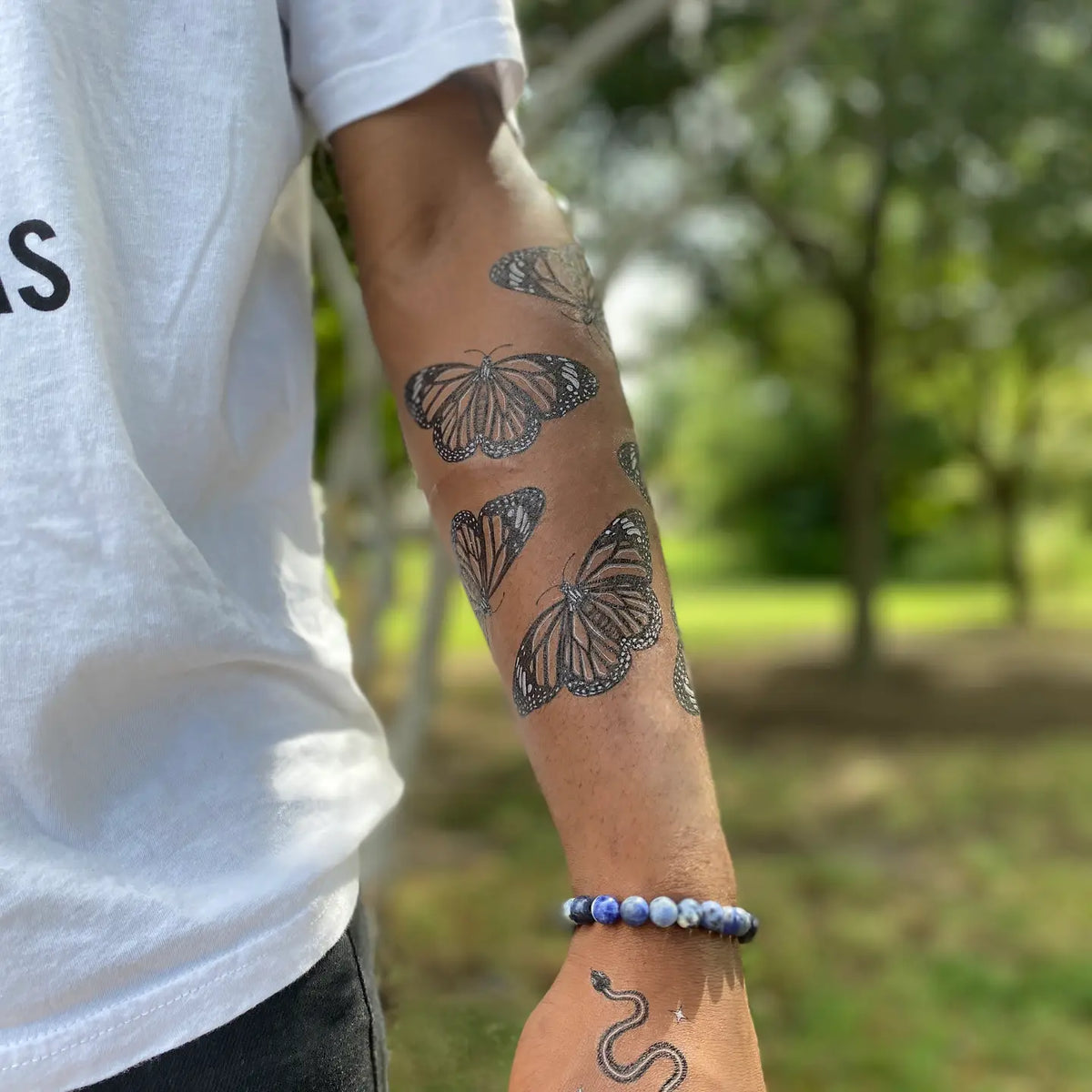 Forearm decorated with several monarch butterfly temporary tattoos in black line art.