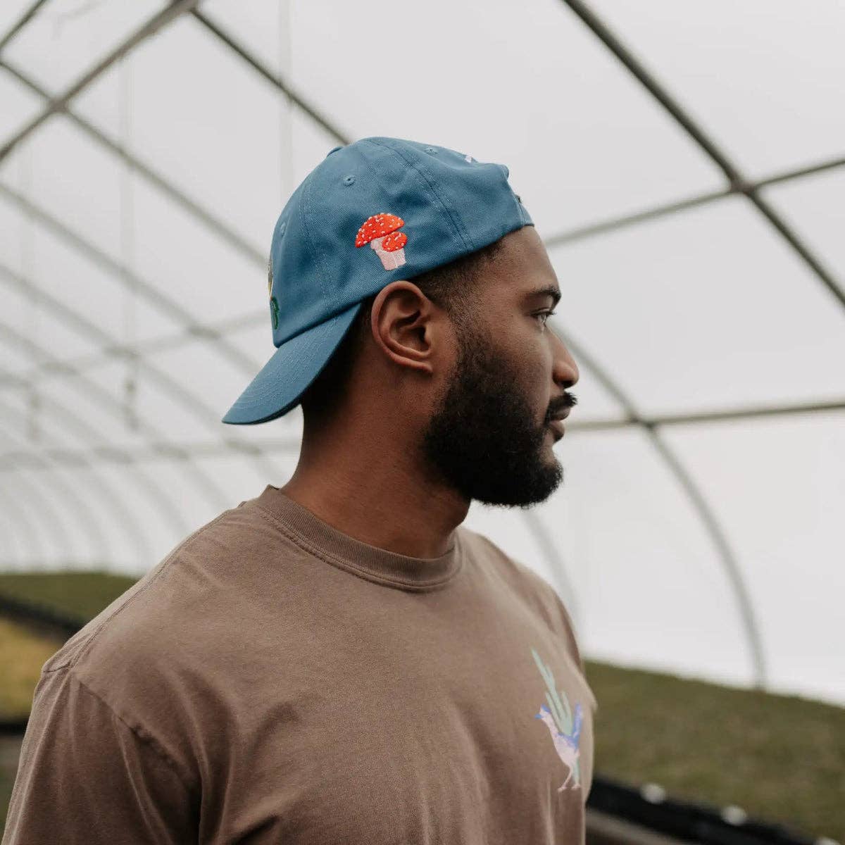 Profile view of a man wearing a blue Eastern Native Flora & Fauna Hat with red mushroom embroidery.