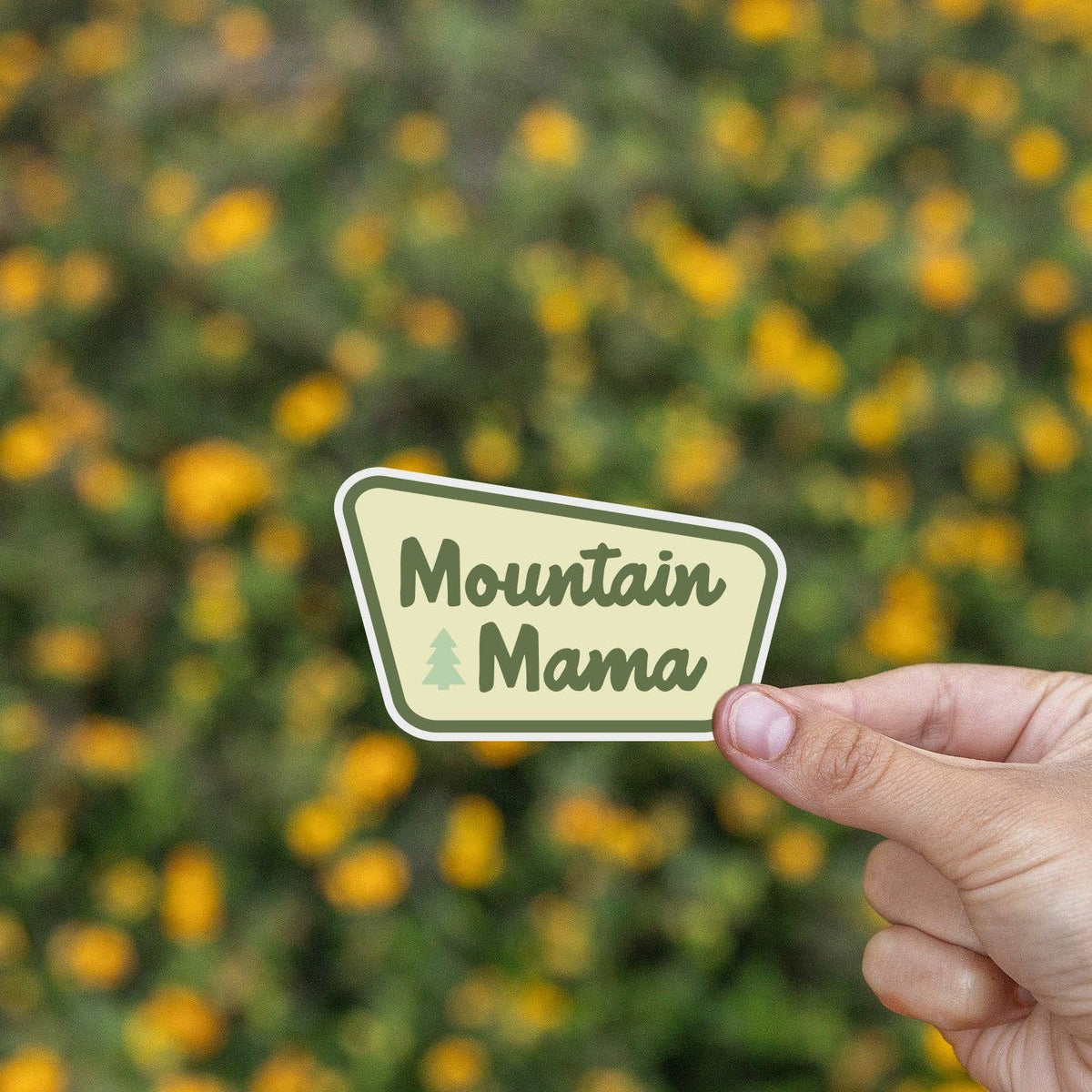Mountain Mama sticker on a red Hydro Flask with a blurred field of yellow flowers in the background