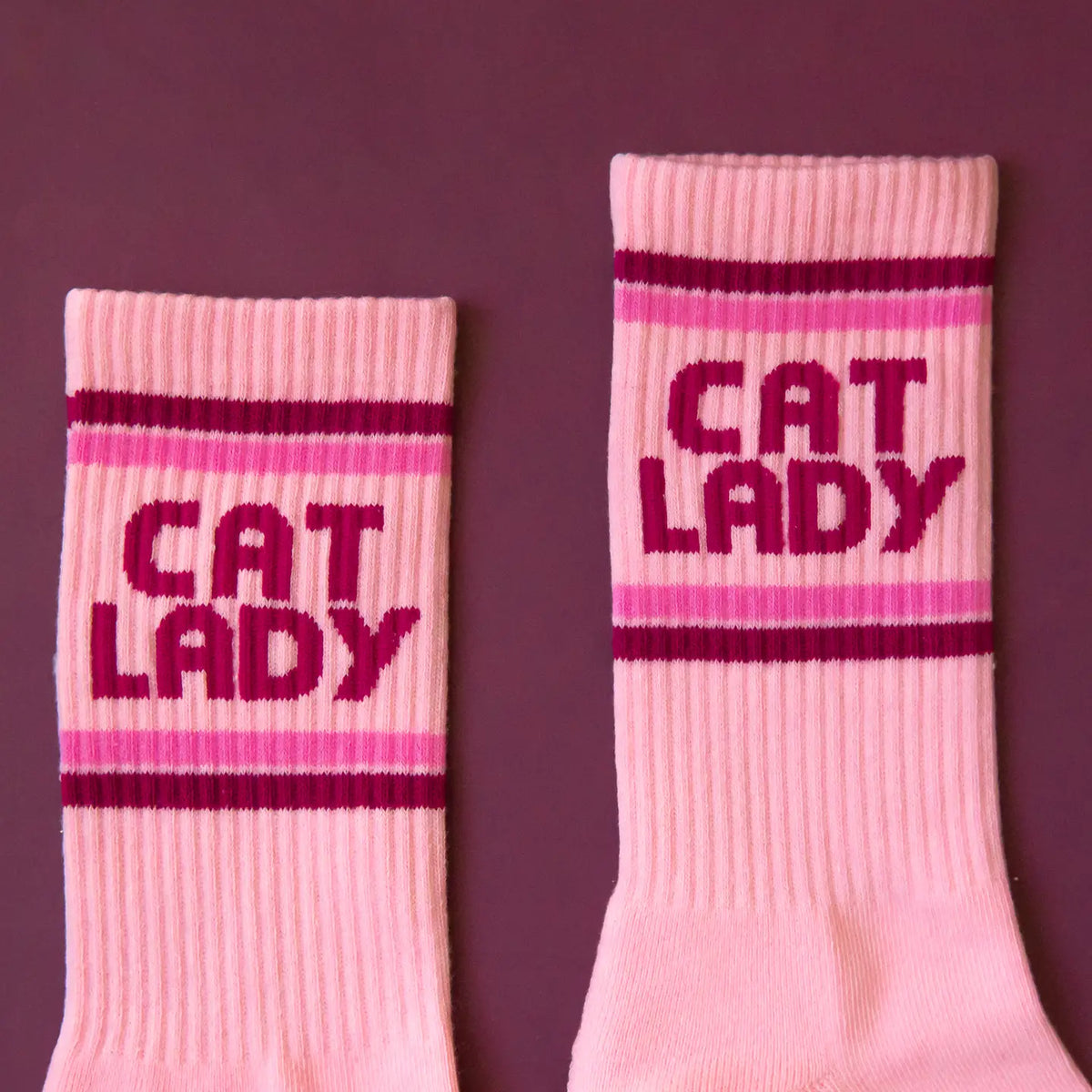 Pink ribbed crew socks with CAT LADY lettering and stripe details on a mauve background.