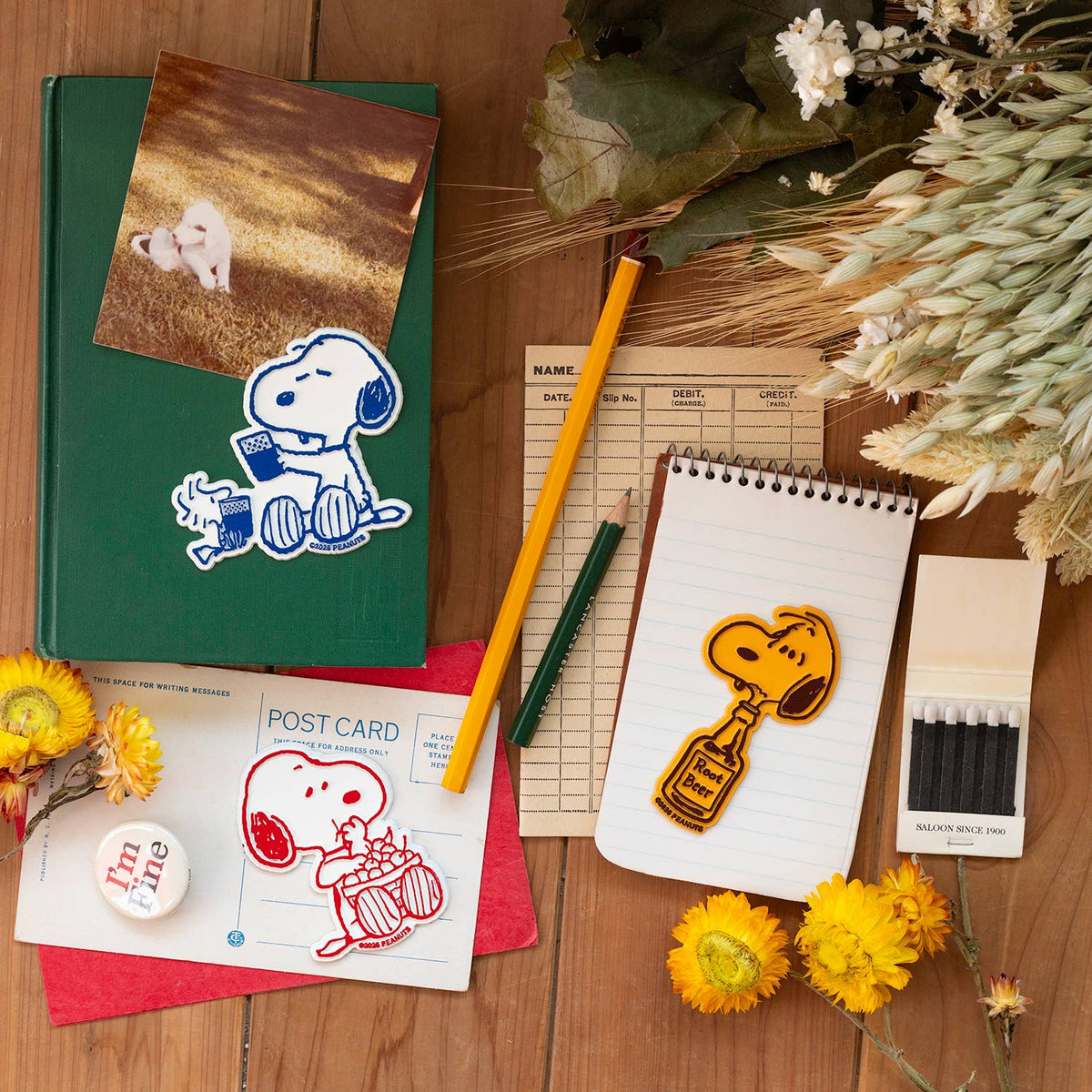 Snoopy root beer magnet on a green binder beside a photo and school supplies