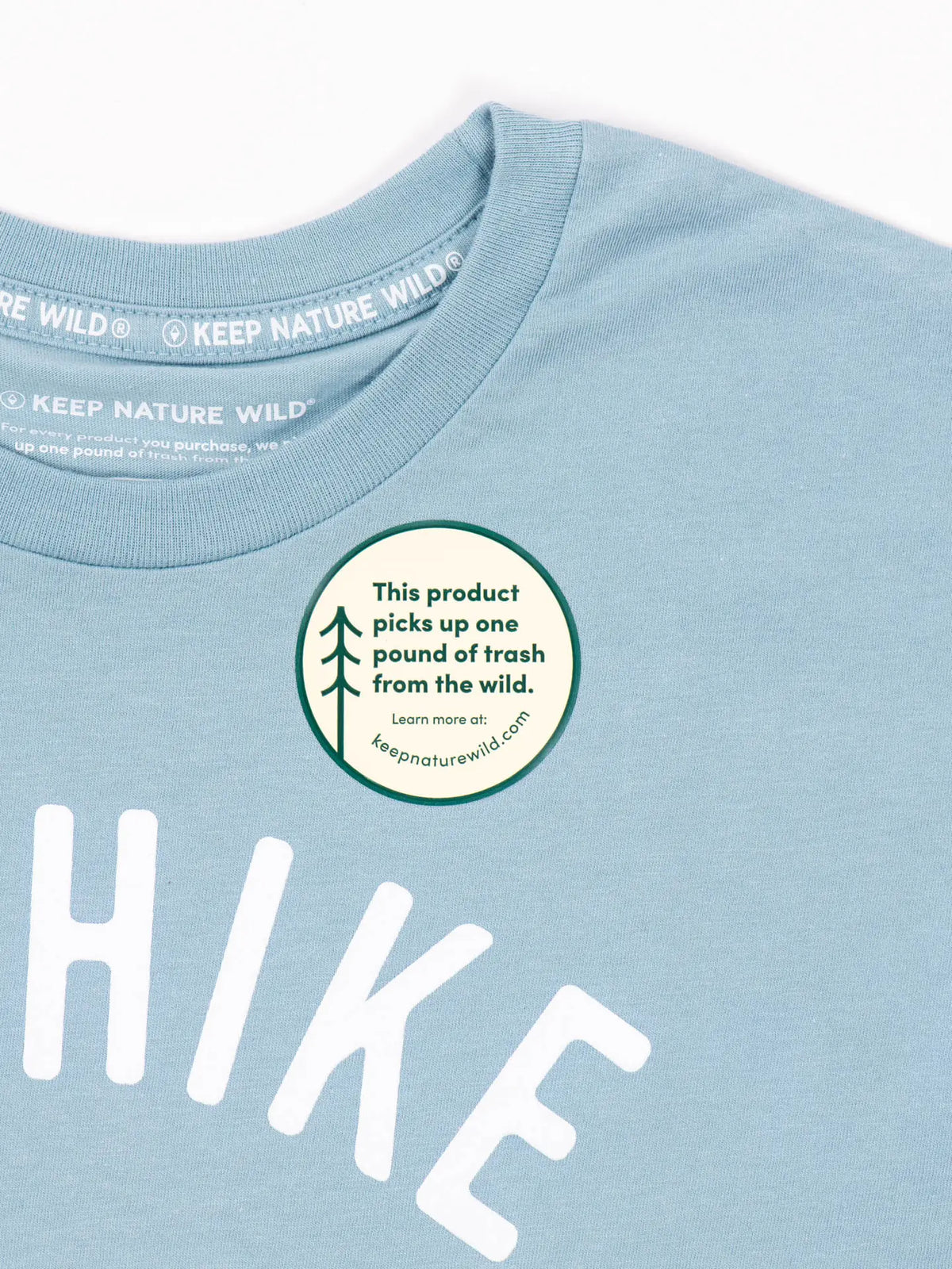 Close up of a light blue I'd Hike That tee showing a white KEEP NATURE WILD neck label and a round sticker.