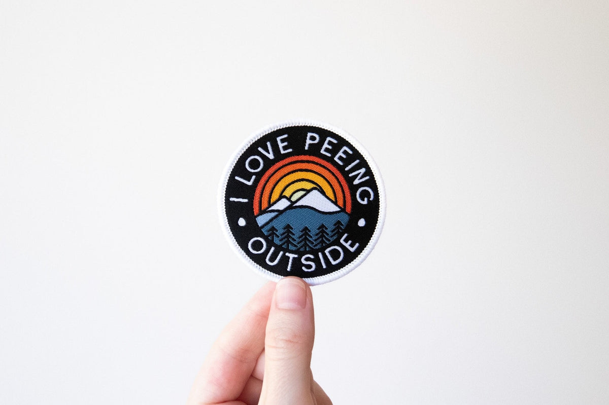 Circular patch with black background rainbow mountain design and the text I love peeing outside