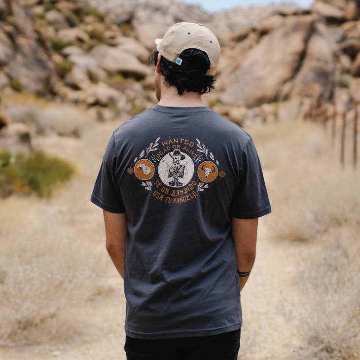 Model wearing a dark Dead or Alive t shirt outdoors in a desert setting with the back graphic visible.