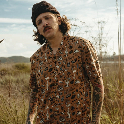 Man wearing Raise Hell Eat Tacos casual button-up shirt outdoors in a desert field.