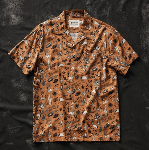 Flat lay of Raise Hell Eat Tacos casual button-up shirt in brown with scattered taco and desert icons on black background.