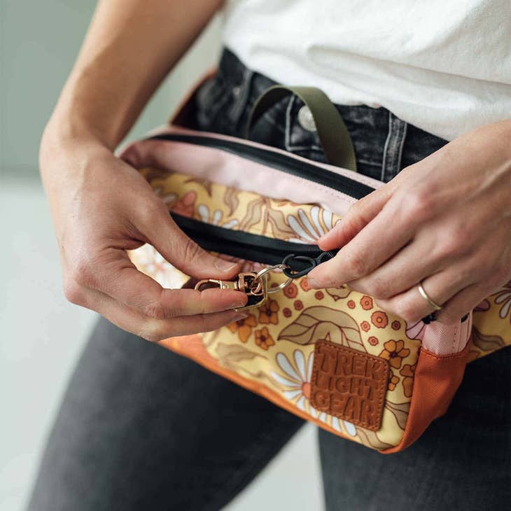 Person wearing pink floral fanny pack around the hip with adjustable strap and black zipper.