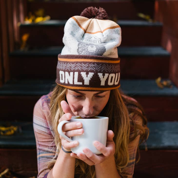 Woman wearing the Only You Smokey Bear beanie while sipping coffee on outdoor steps