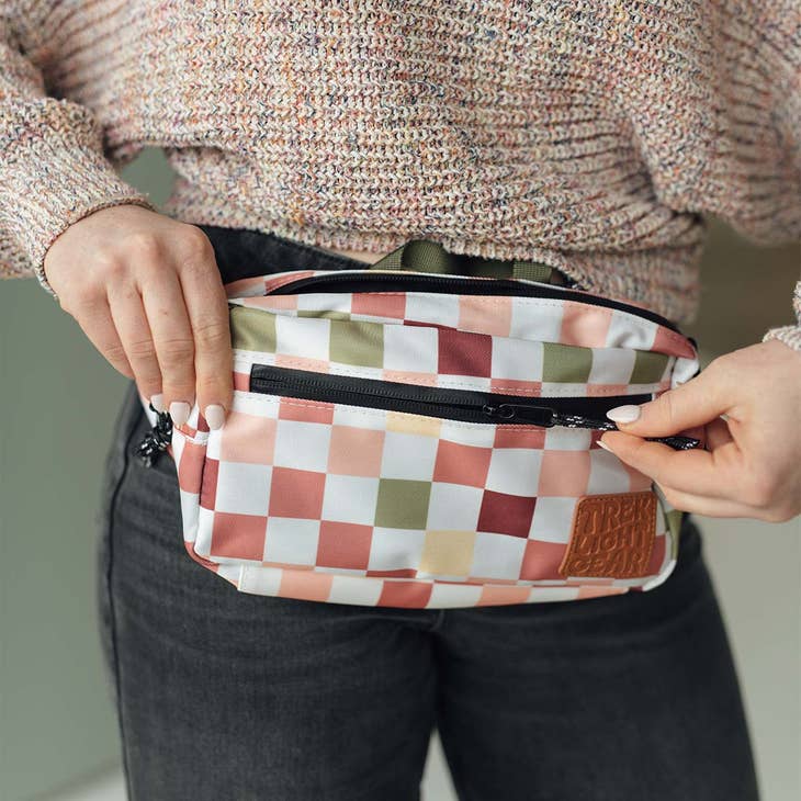 Person wearing the checkers pattern Everyday Fanny Pack around the waist while opening the front zipper