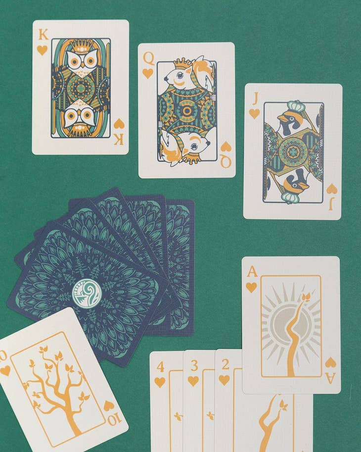 Face cards with forest motifs King Queen Jack and a fan of blue backed cards on a green table.