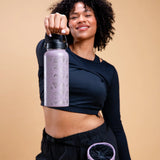 Lavender reusable water bottle with triangular park sticker pattern held up by a woman in dark athletic wear.