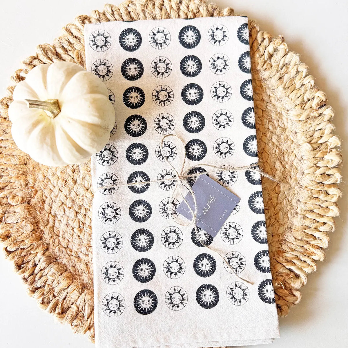 Cotton sun tea towel laid on a woven placemat with a small white pumpkin and twine wrapped tag