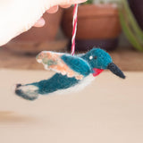 Teal felt hummingbird ornament with orange and white wings and red throat hanging from pink and white thread.