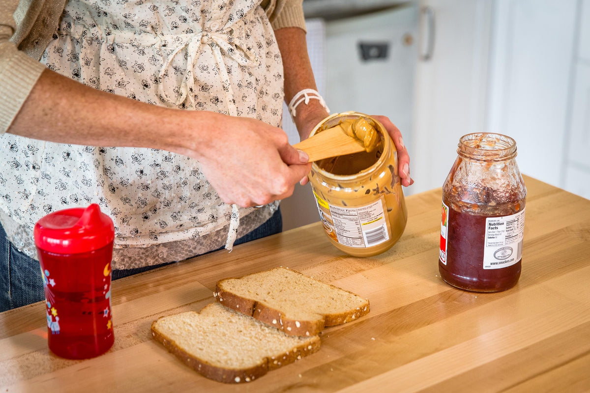 Hands with a wooden spreader scooping prickly pear marmalade from a jar onto bread