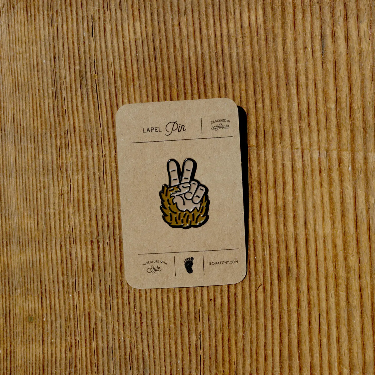 Bigfoot Peace Sign enamel pin attached to tan lapel pin display card