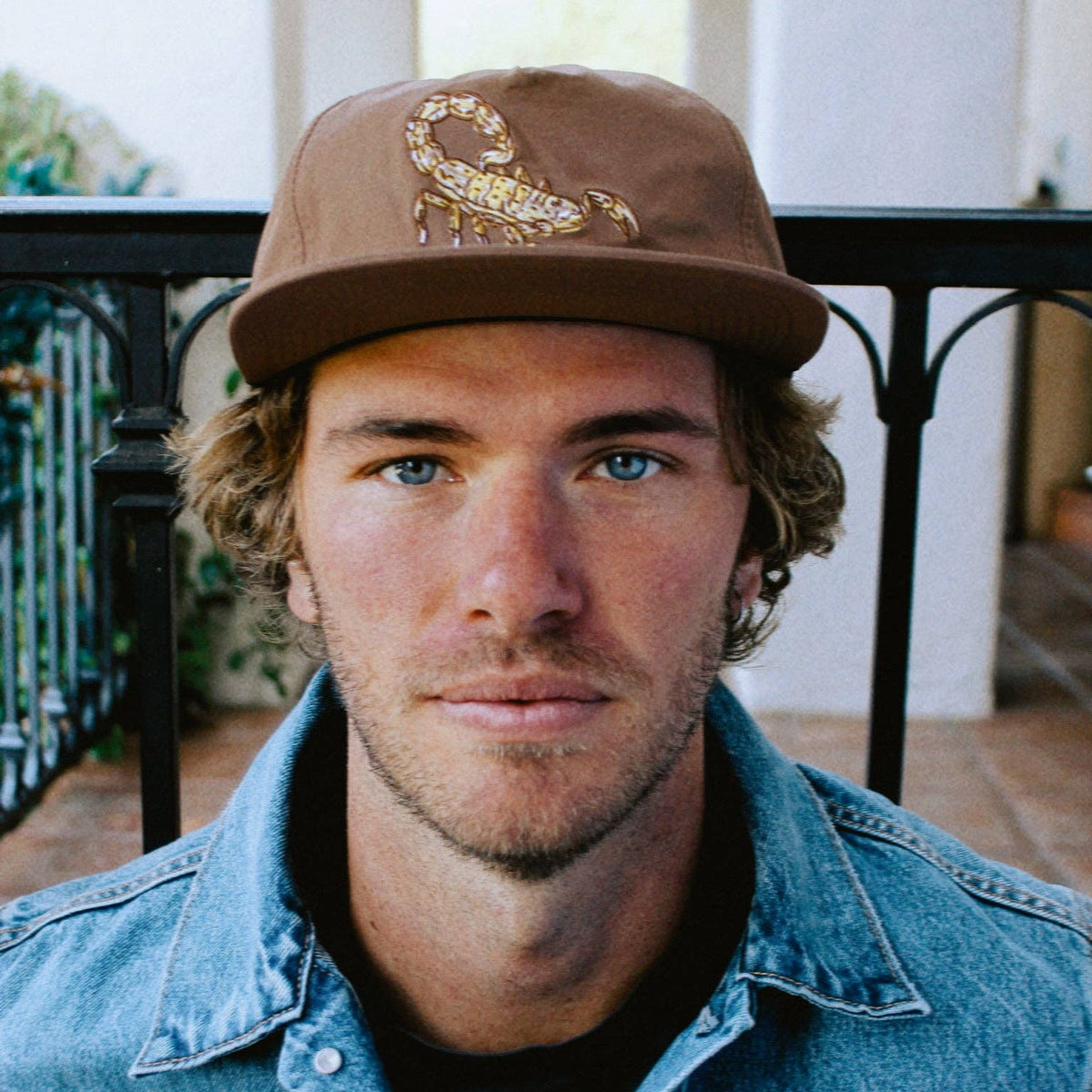 Person wearing brown Scorpion Hat with embroidered scorpion on the front and a denim jacket