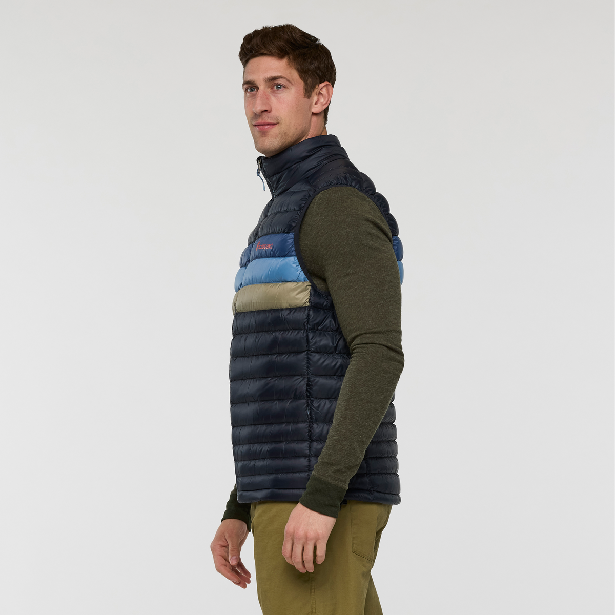 Side view of a man wearing Cotopaxi Fuego Down Vest with navy and striped panels over an olive green sweater