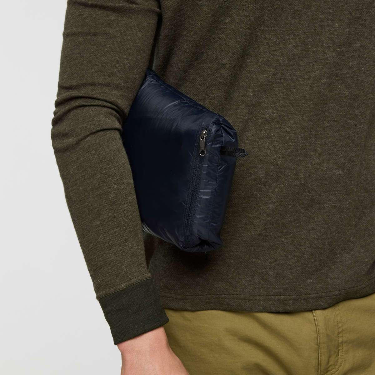 Side view of the navy packable pocket on the Cotopaxi Fuego Down Vest worn with an olive sweater.