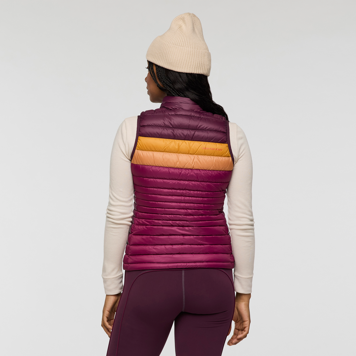 Back view of a woman wearing Cotopaxi Fuego Down Vest in purple with orange amber chest stripe.