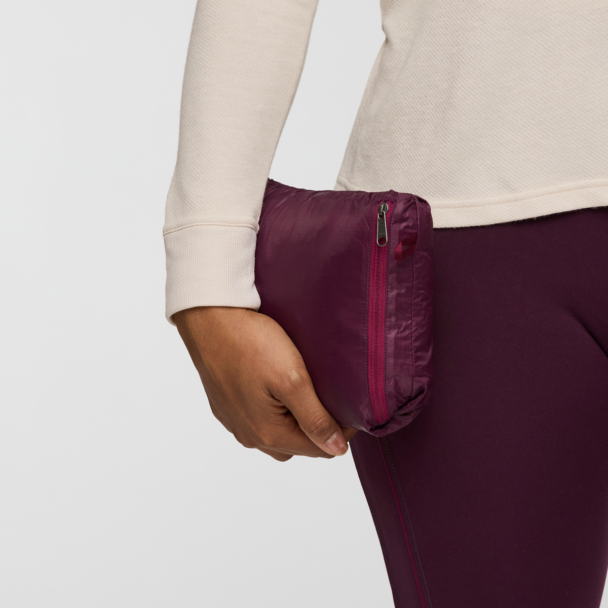 Hand holds a compact zippered packable pouch in deep plum from the Cotopaxi vest