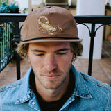 Man wearing brown Scorpion Hat with gold embroidered scorpion on the front.