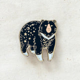 Moon Bear enamel pin featuring a dark bear with starry pattern and pale muzzle on light fabric background