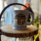 Arizona blue glaze mug with handle and desert logo resting on a wooden slice