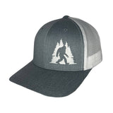 Charcoal trucker hat with white embroidery of a Bigfoot silhouette between pine trees on the front panel and a light gray mesh back.