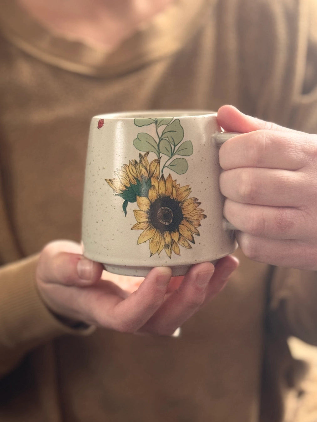Cream speckled sunflower mug held by hands showing side view with handle and green leaf interior